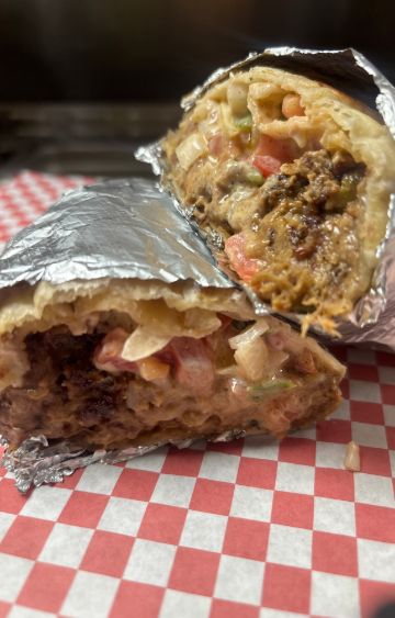 Both halves of a foil-wrapped burrito, cut open to show meat, diced tomato and onion in a creamy sauce, on red and white checkered paper