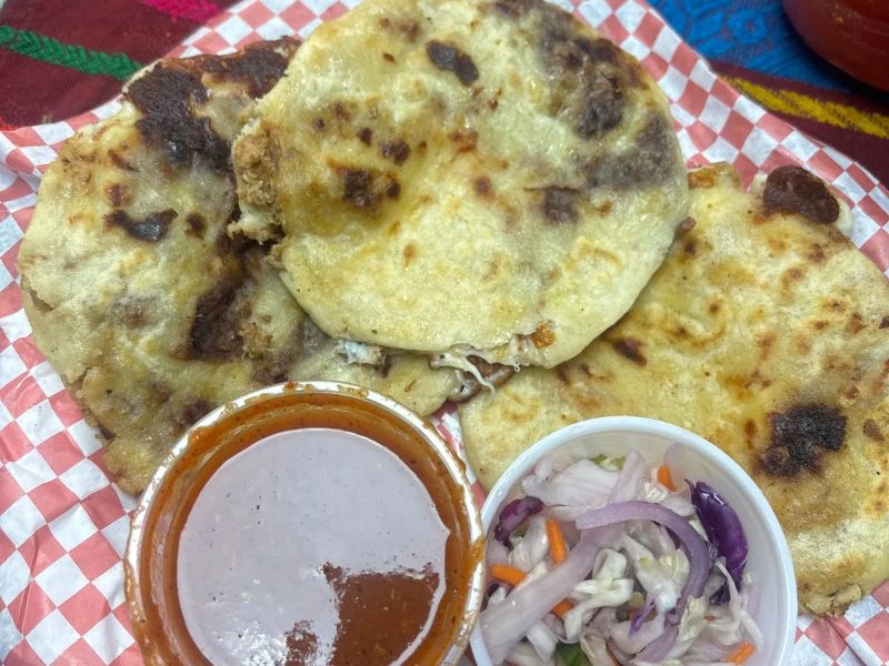 Pupusas on checkered paper with red salsa and curtido