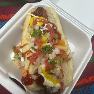 Hot dog topped with tomato, onion, cilantro, mustard and ketchup