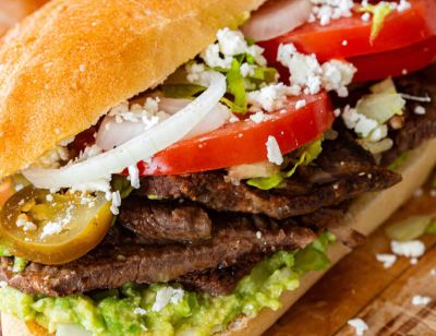 A torta with grilled meat, avocado, tomato, onion, jalapeño and crumbled white cheese